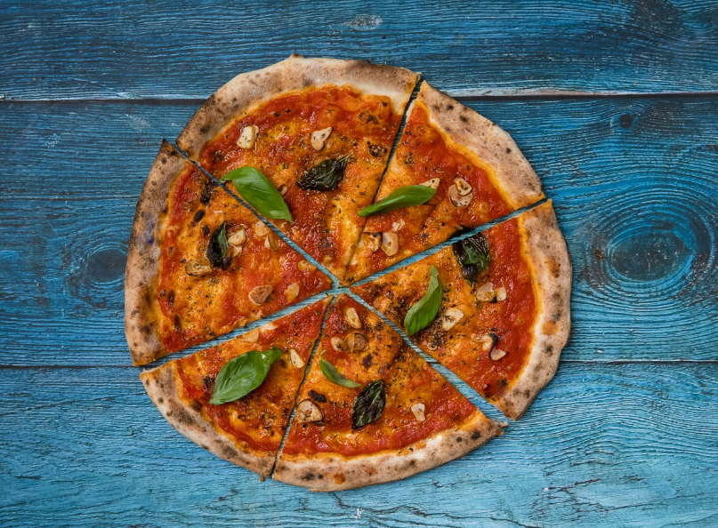 A pizza with basil leaves on a blue wood surfaceDescription automatically generated