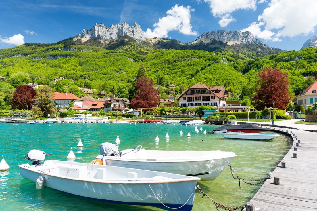 Boats on a body of water with a dock and mountains in the backgroundDescription automatically generated