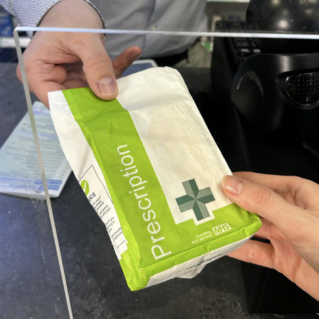 An NHS prescription being handed to a patient at a pharmacy counter