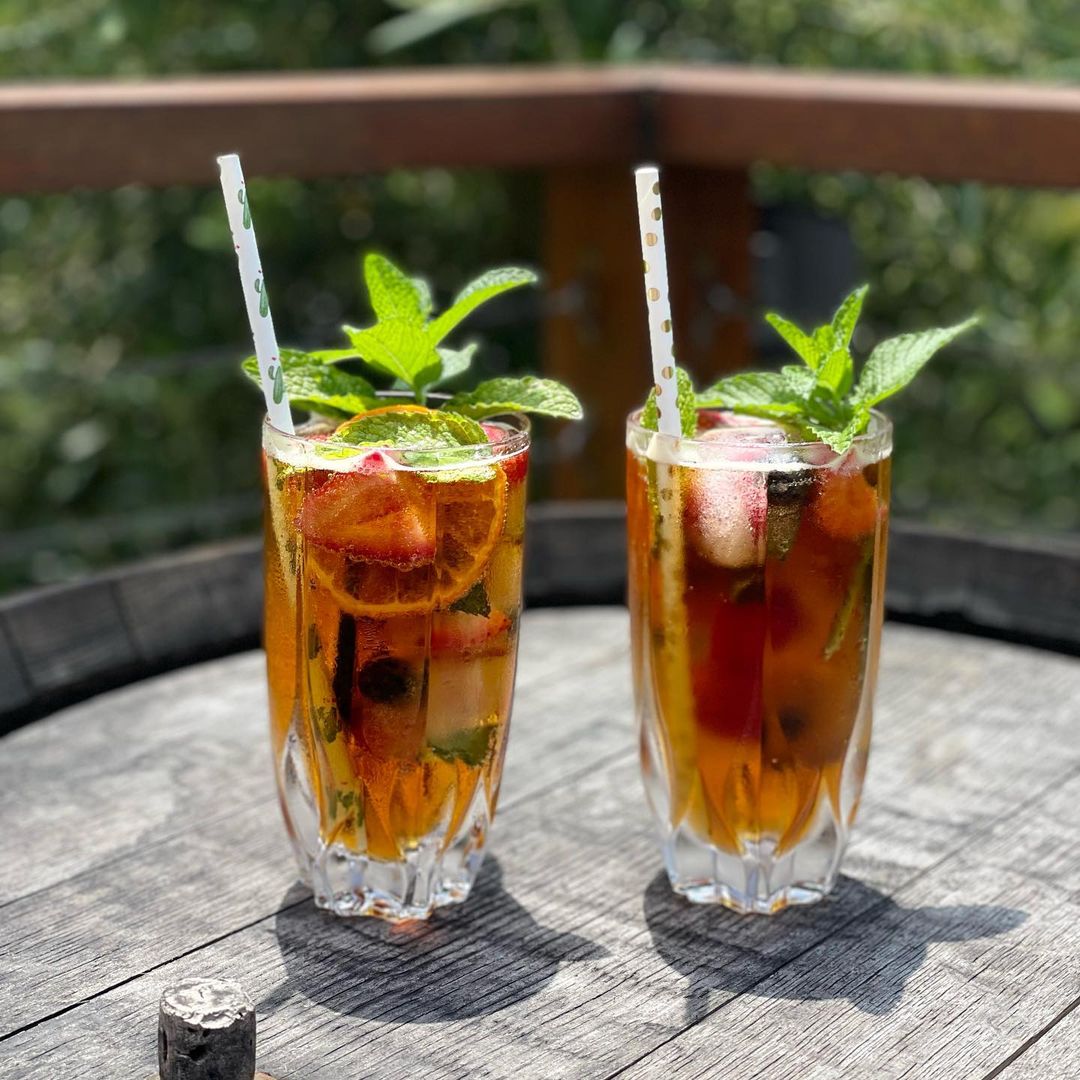 Dark Amber Coloured Pimms in a High Ball Tall Glass. Garnished With Mint & Lemon & Any Other Fruit You Can Find. Drink Through a Straw!