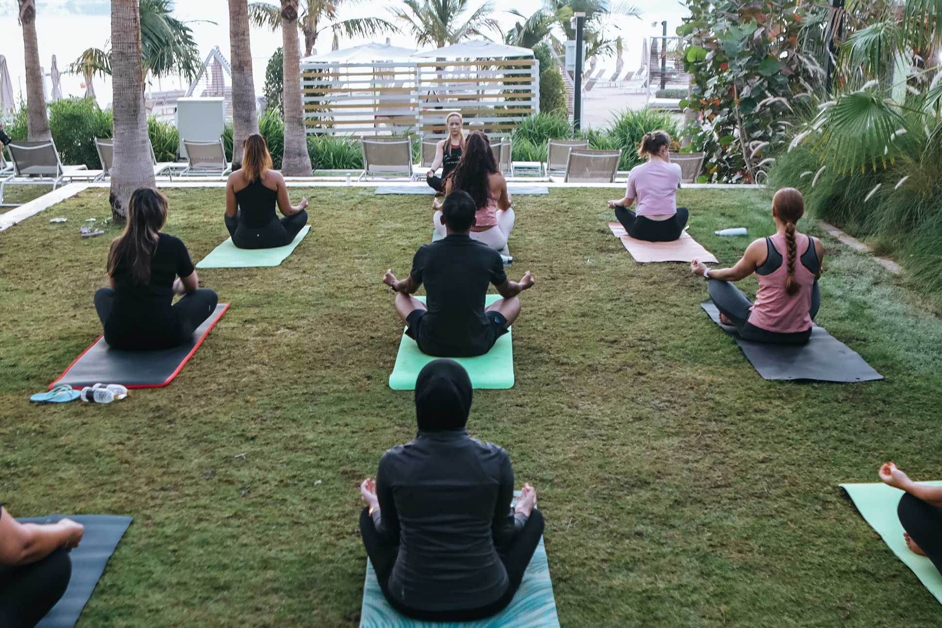 A group of people sitting on mats in a grassy areaDescription automatically generated with medium confidence