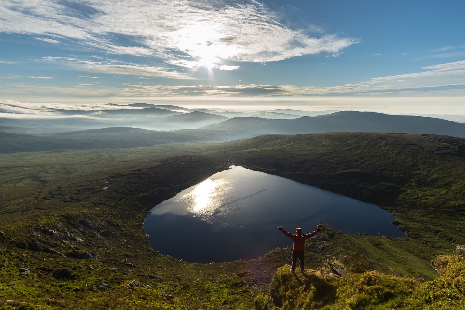 A person standing on a hill with a lake in the backgroundDescription automatically generated