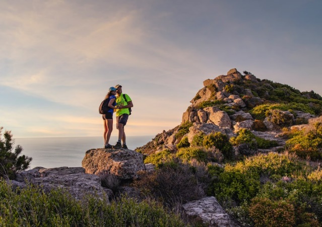 A couple of people standing on a rock overlooking a body of waterDescription automatically generated with low confidence