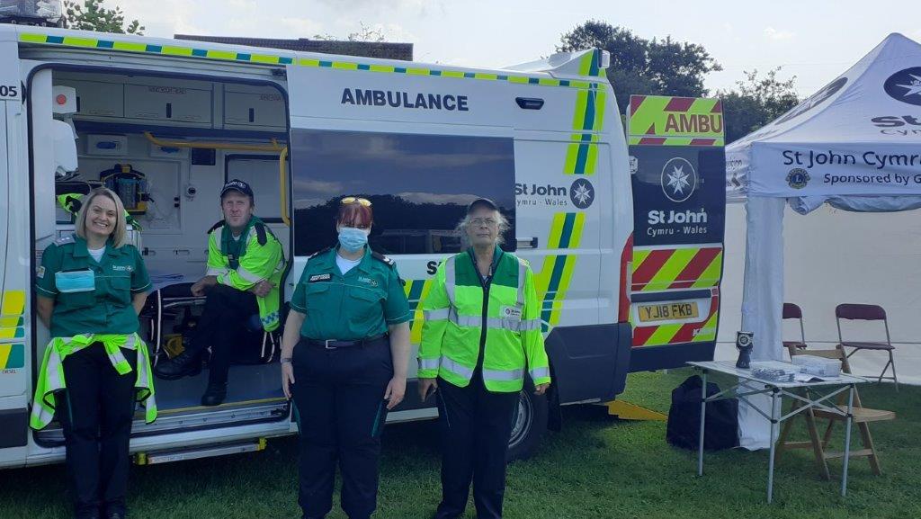 A group of people standing in front of a ambulanceDescription automatically generated