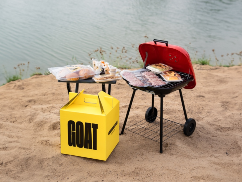 A barbecue grill with food on the sandDescription automatically generated with medium confidence